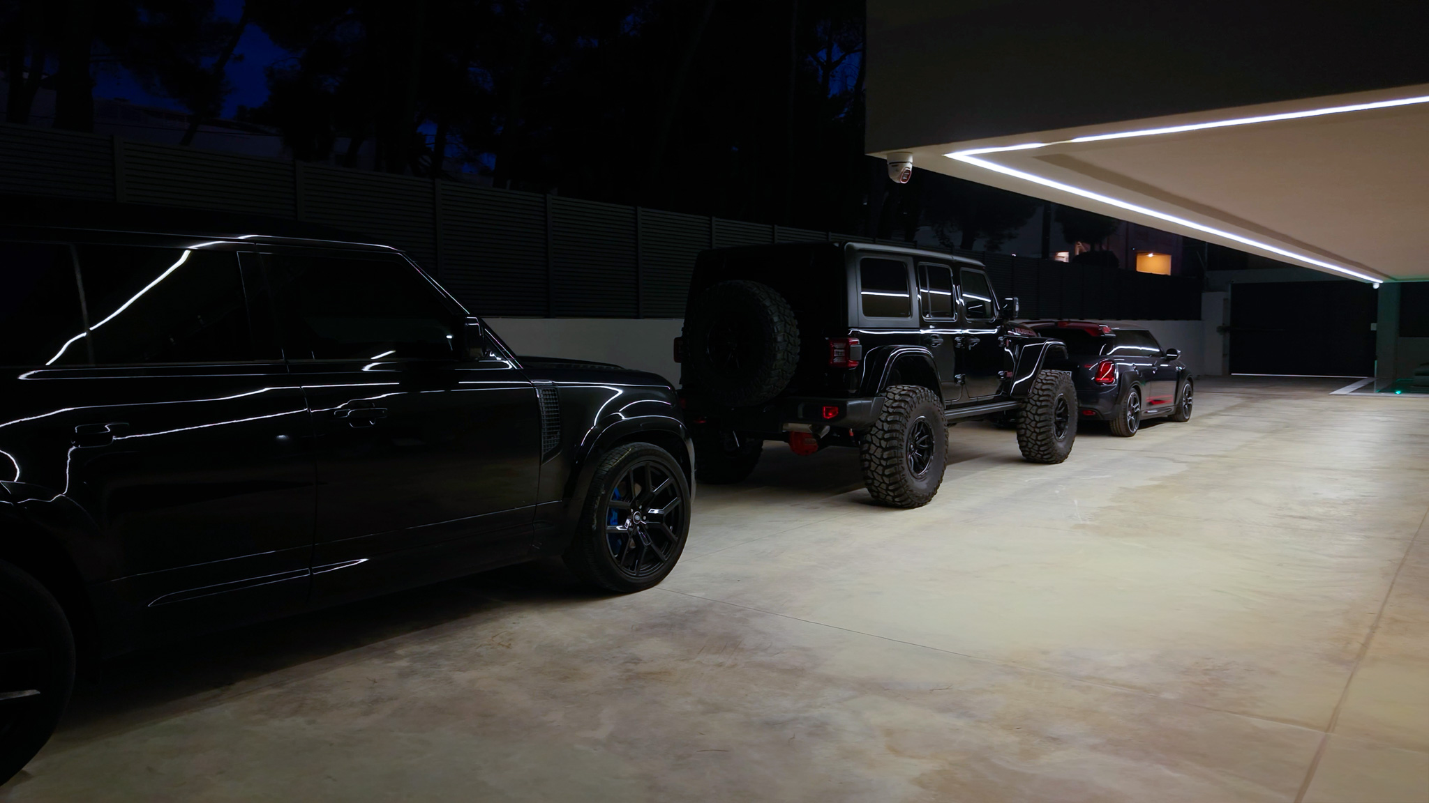 Villa Bond, three black cars under linear LED canopy at night